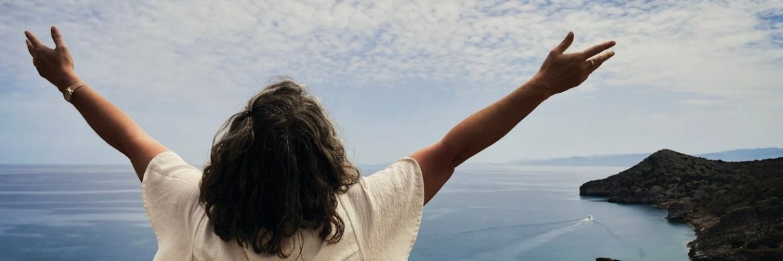 Woman with arms outstretched overlooking the ocean.
